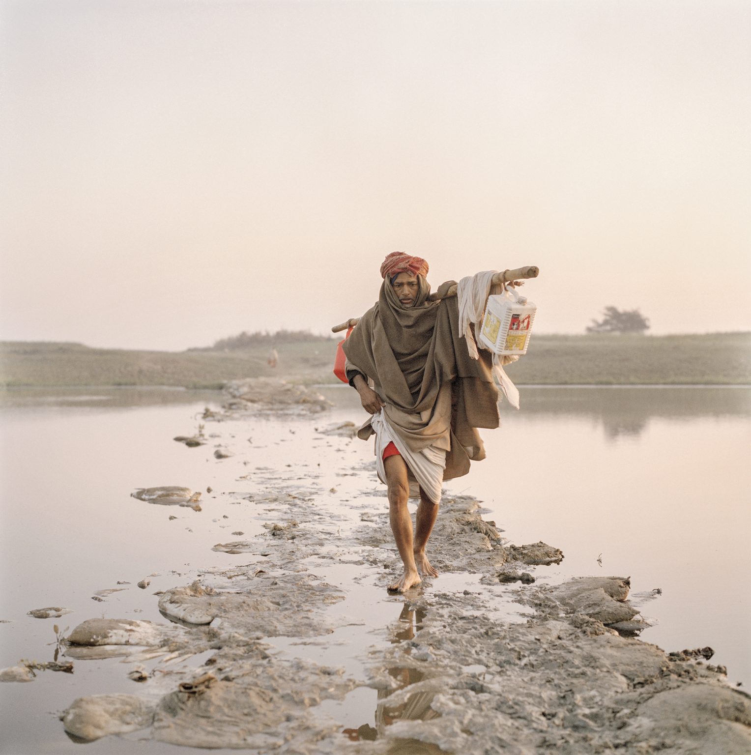 An eldery man crosses a small channel of the Ganges on a submerging bridge made of waste, 2014.