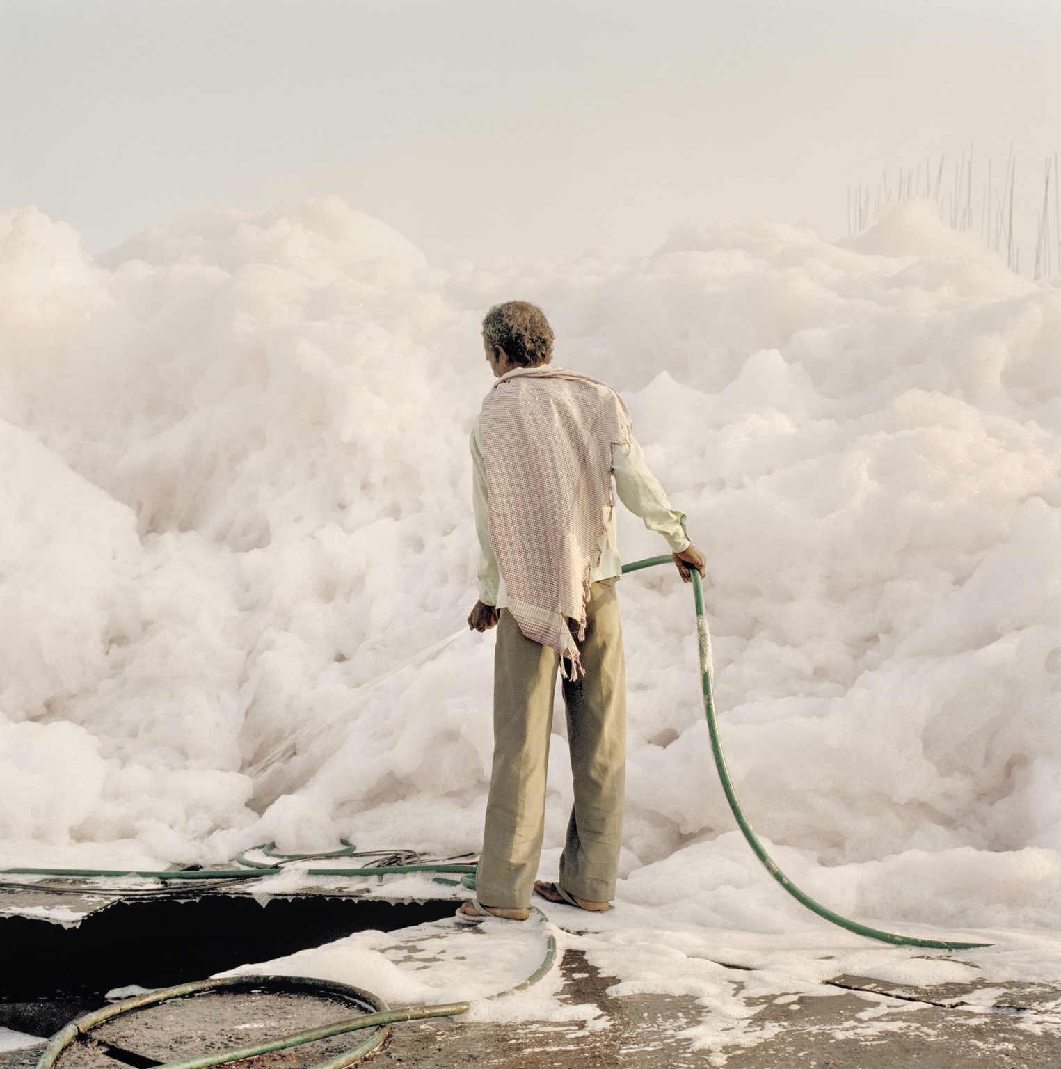 A worker with a water hose tries to tame an iceberg of foam form chemical waste dumped by factories along the Yamuna river.