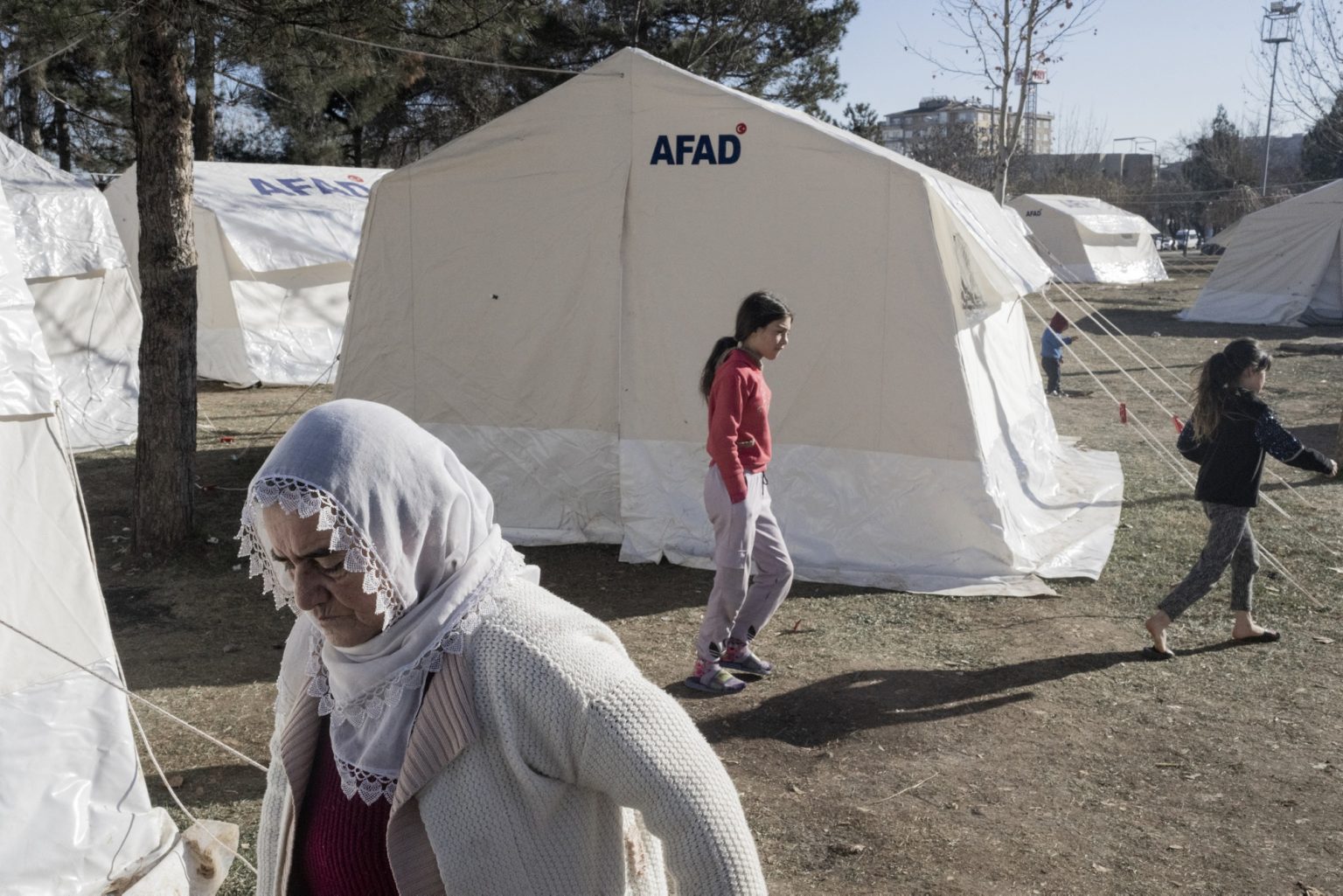 Diyarbakir, Turkey, February 2023 - The aftermath of the earthquake that hit southern Turkey and northern Syria.  A woman and girls walk in a tent camp set up in the city of Diyarbakir.><
Diyarbakir, Turchia, febbraio 2023  Le conseguenze del terremoto che ha colpito la Turchia del Sud e la Siria del nord.